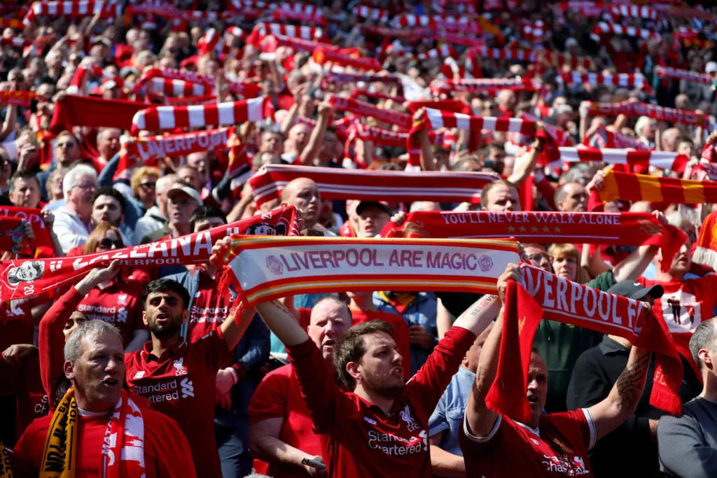 Distesa di tifosi del Liverpool con le sciarpe rosse e bianche alzate; in primo piano una sciarpa con la scritta "Liverpool Are Magic", sugli spalti migliaia di persone in rosso.