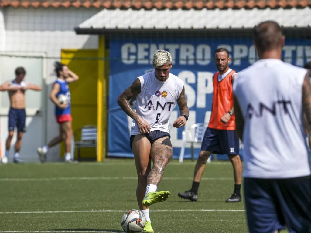 Giocatori in maglia bianca e pettorina arancione durante un allenamento, un uomo di spalle in primo piano. Michele Calvanese — Rangers Qualiano — SPORTSHOTS Magazine