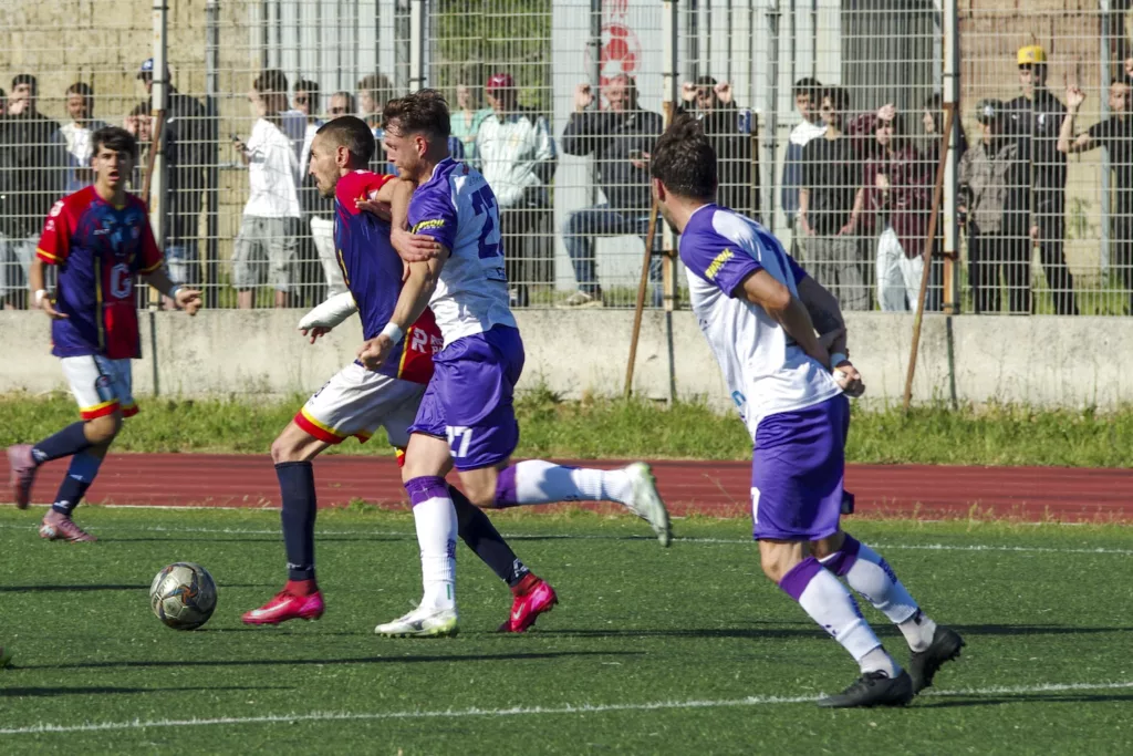 Giocatore in maglia bianca salta sopra un compagno in pettorina arancione davanti a un grande striscione blu. Michele Calvanese — Rangers Qualiano — SPORTSHOTS Magazine