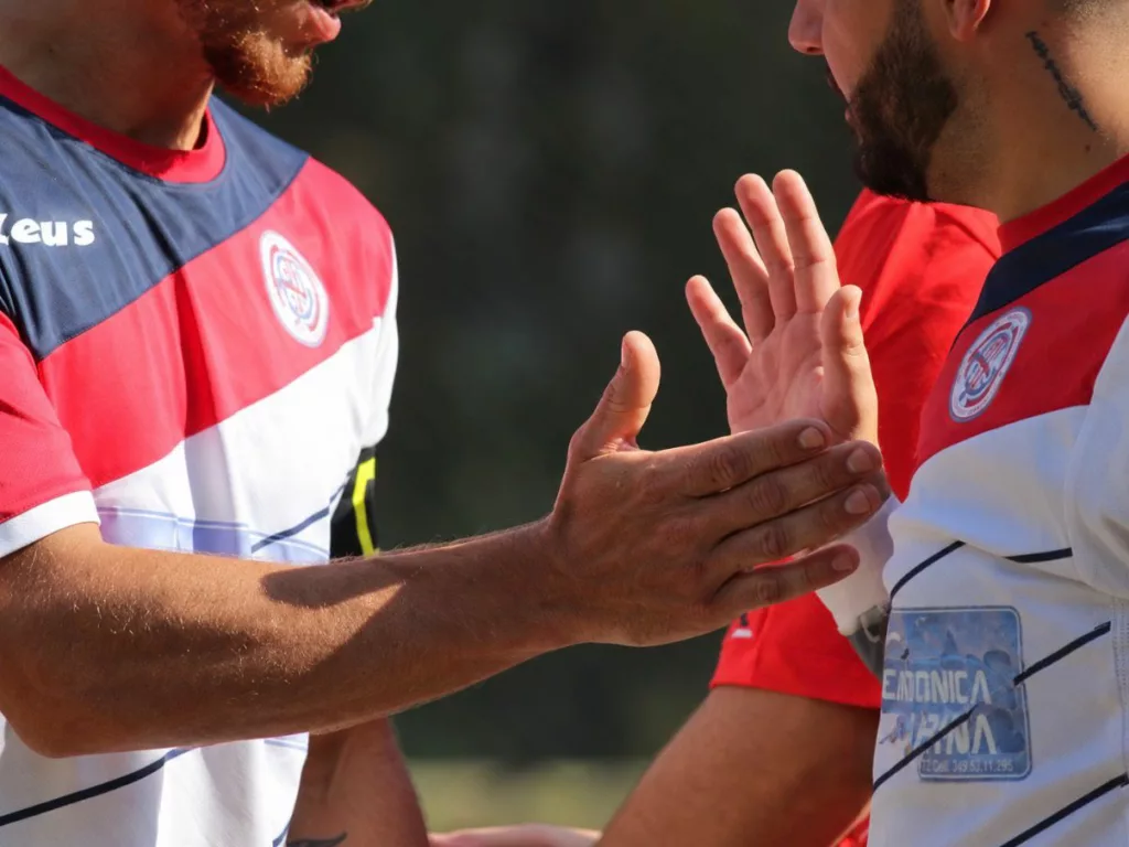 Primo piano di due giocatori in maglia rossa e bianca che si stringono la mano. Sofia Gasbarri — ASD Montorio Romano — SPORTSHOTS Magazine
