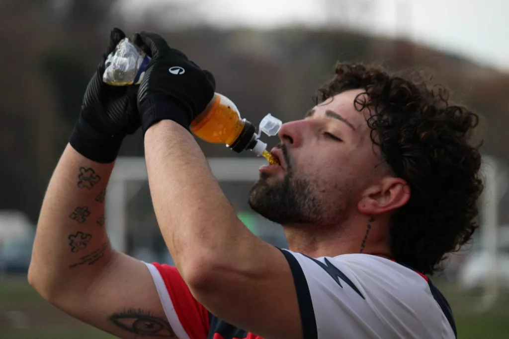 Giocatore con guanti neri che beve da una bottiglia a bordo campo. Sofia Gasbarri — ASD Montorio Romano — SPORTSHOTS Magazine