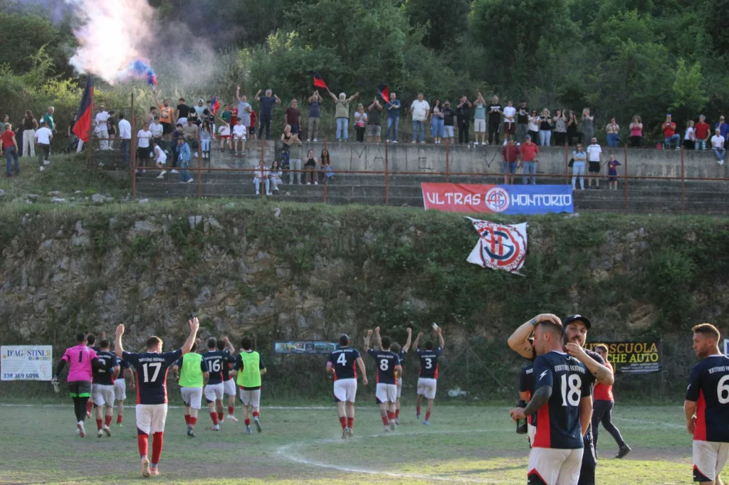 Squadre in campo con il pubblico sulla scarpata sopra il campo, fumo colorato sulla sinistra. Sofia Gasbarri — ASD Montorio Romano — SPORTSHOTS Magazine
