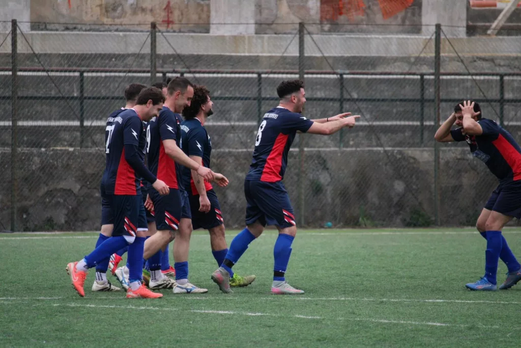 Gruppo di calciatori in maglia blu e rossa che camminano insieme sul terreno di gioco. Sofia Gasbarri — ASD Montorio Romano — SPORTSHOTS Magazine