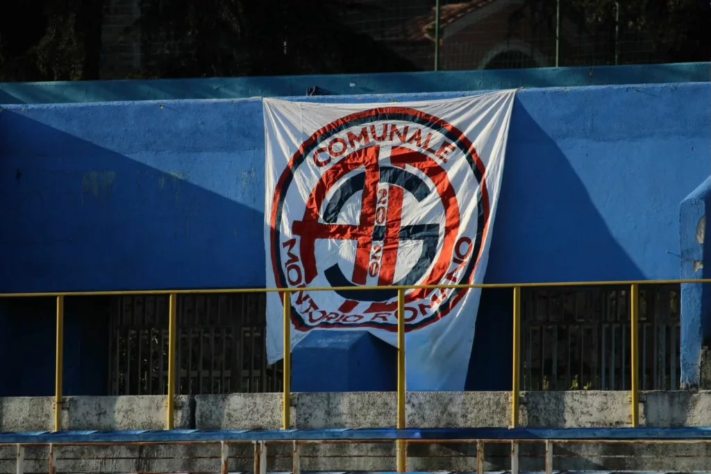 Striscione con lo stemma della squadra appeso a una parete blu. Sofia Gasbarri — ASD Montorio Romano — SPORTSHOTS Magazine
