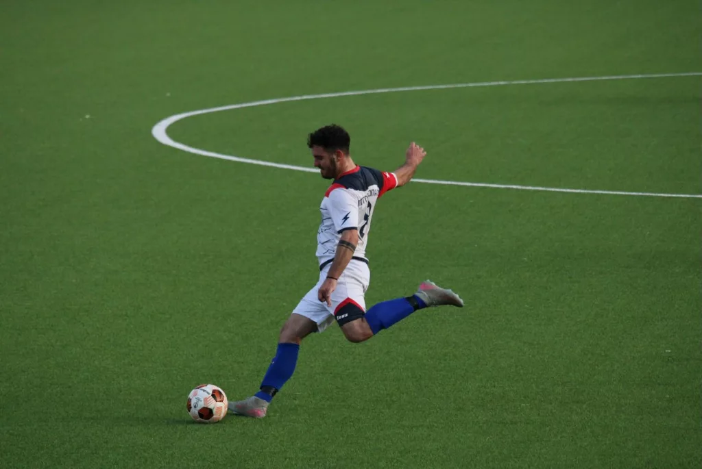 Calciatore in maglia bianca e blu nel gesto del tiro, linea del cerchio di centrocampo sullo sfondo. Sofia Gasbarri — ASD Montorio Romano — SPORTSHOTS Magazine